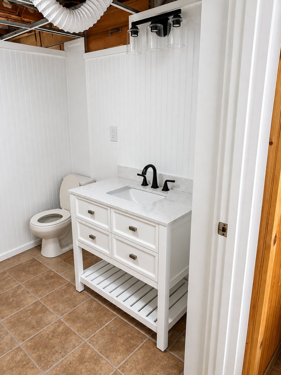 Completed bathroom conversion with white vanity, black fixtures and toilet